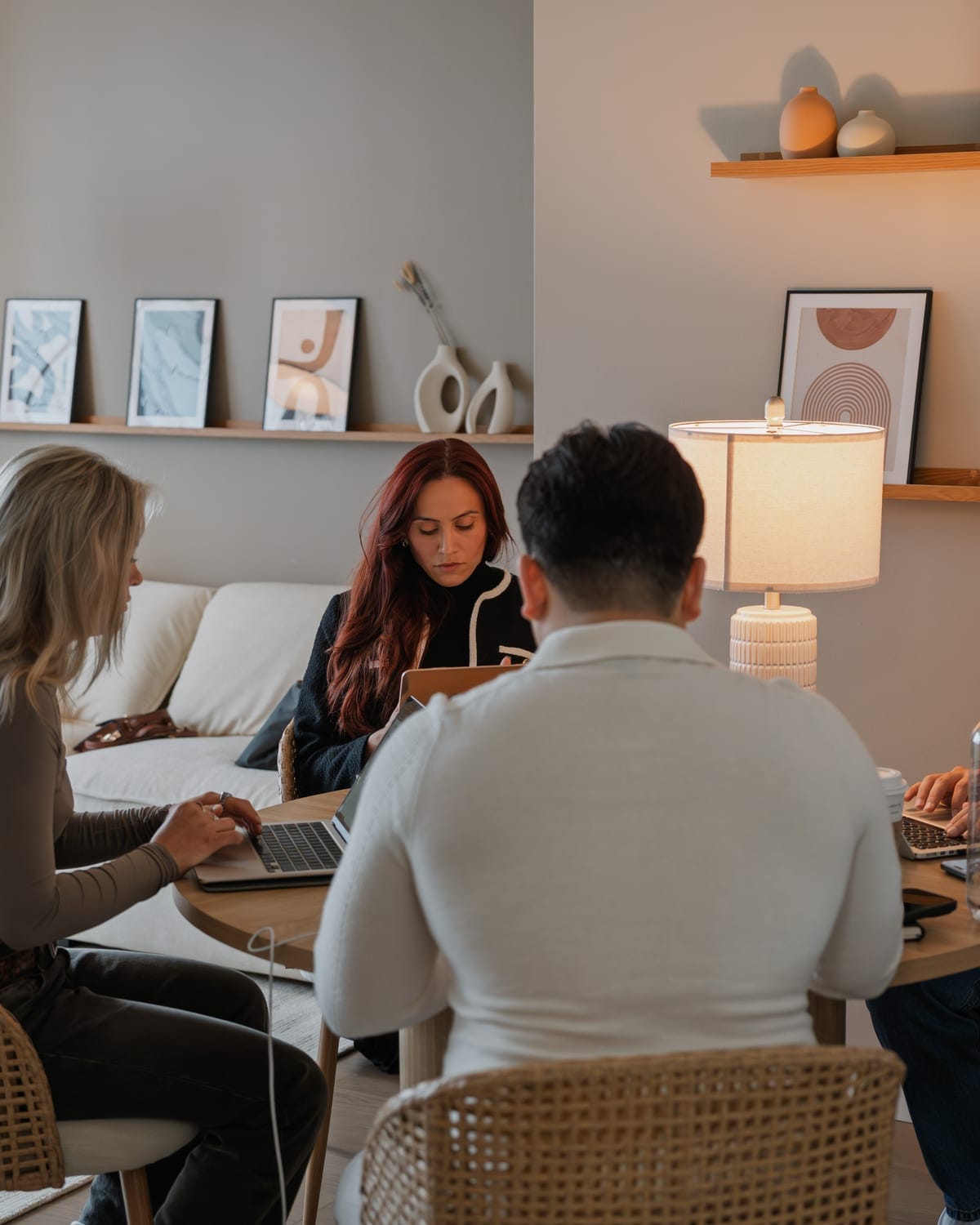 Three people gathered around a dining table beside sofa and display shelves