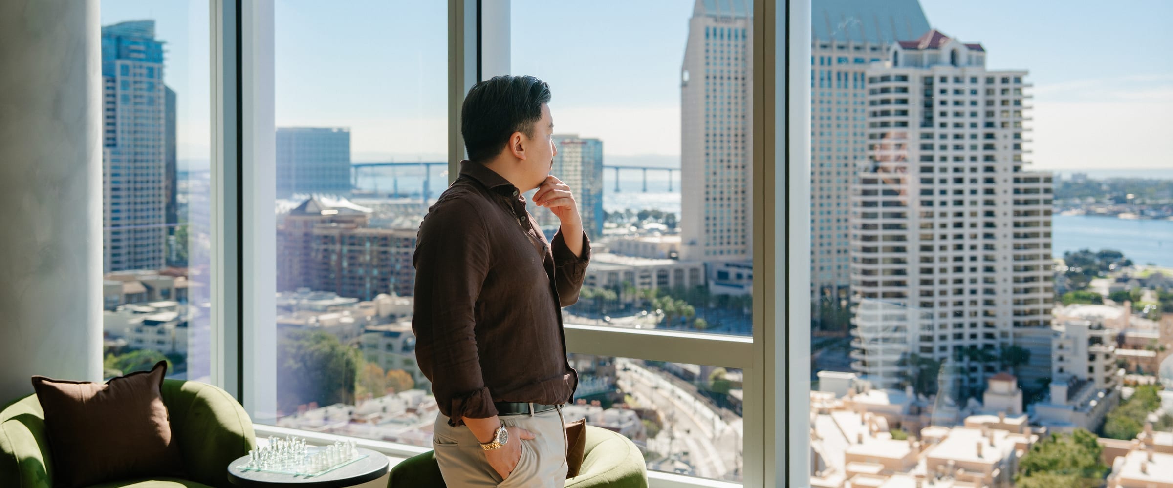 Person standing beside floor-to-ceiling windows overlooking residential towers and water in the distance