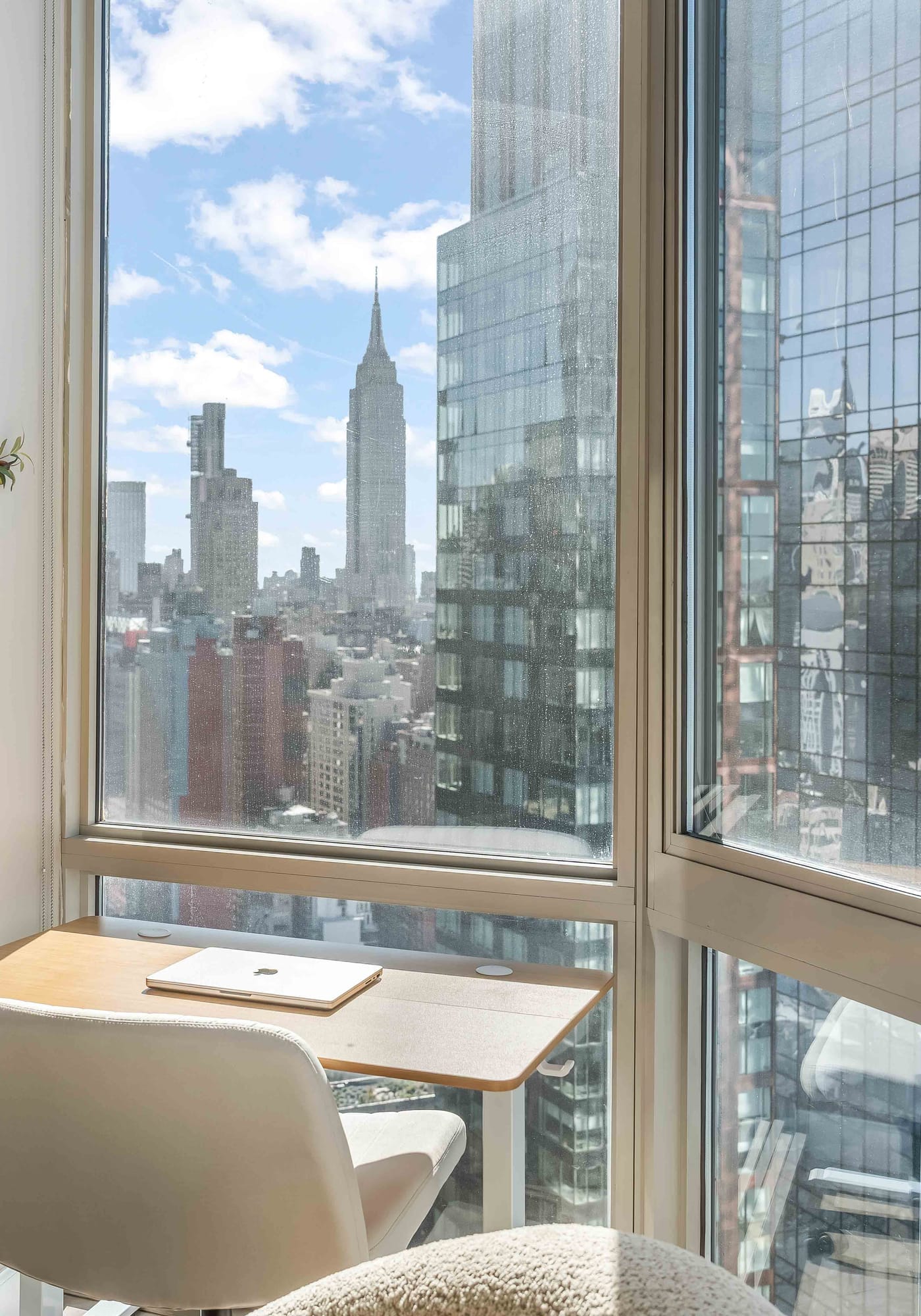 Desk and chair beside corner windows overlooking surrounding glass towers and skyline