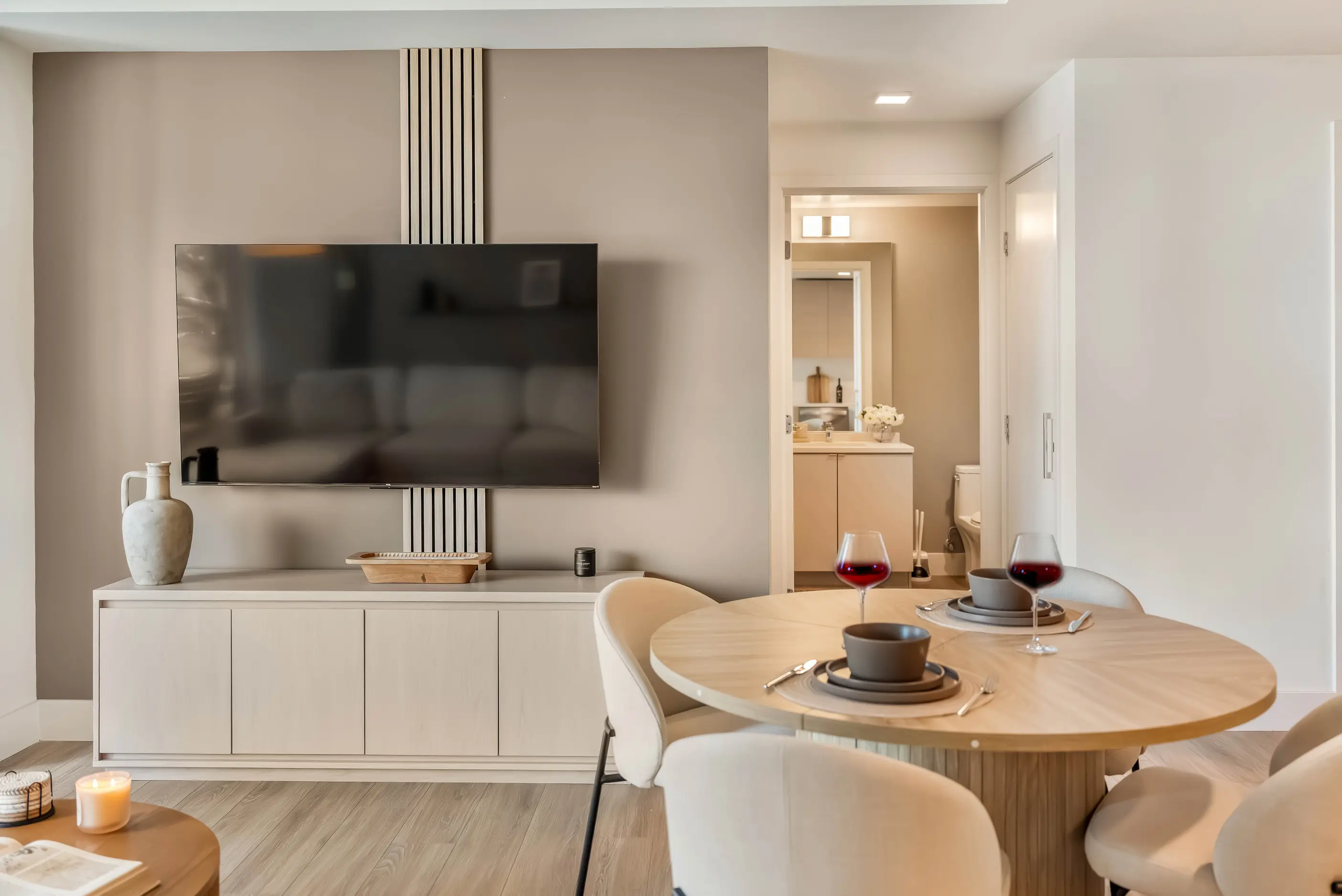 Dining table with upholstered chairs facing wall television above white console at The Palazzo in San Diego