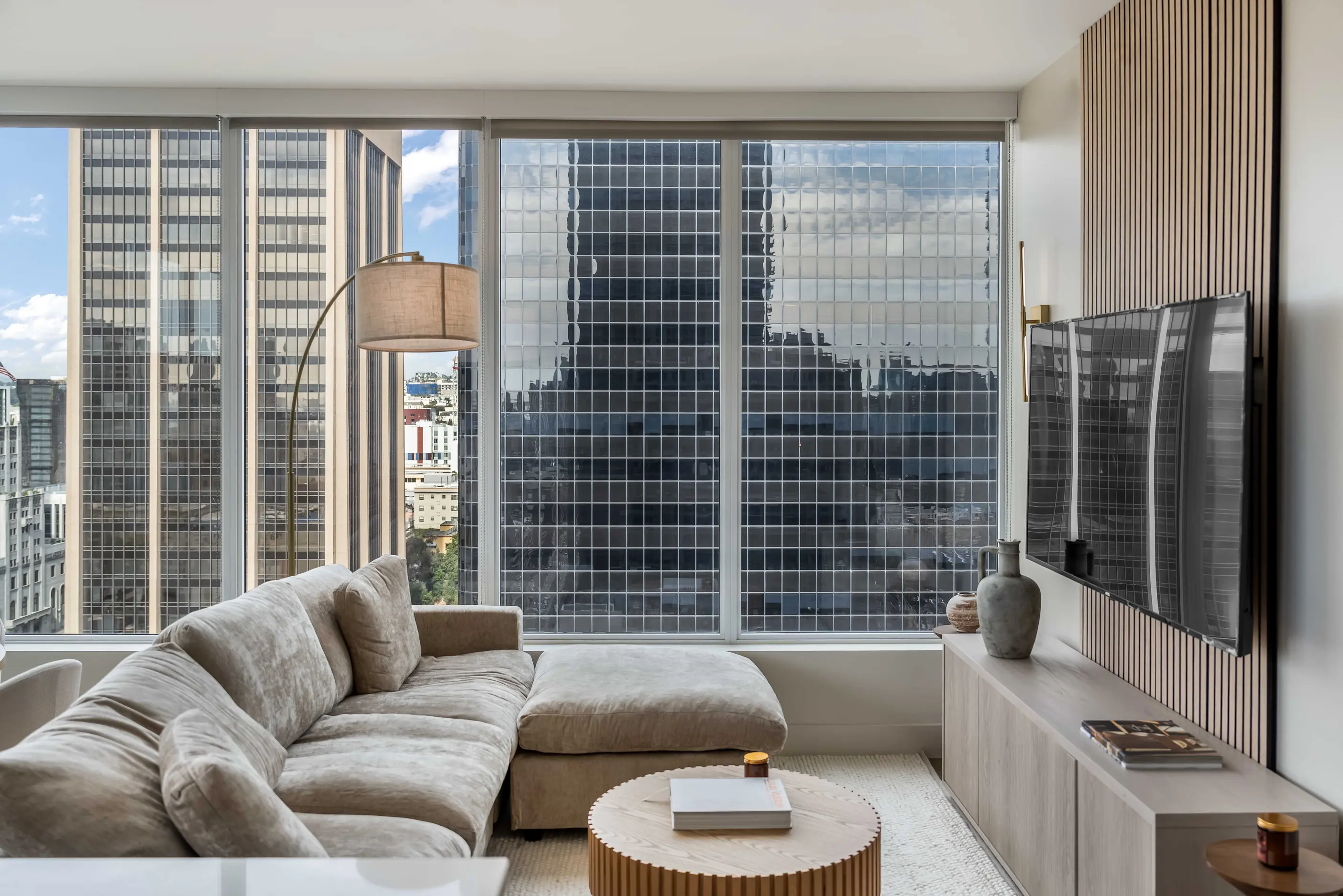 Gray sectional sofa facing television beside round wooden table beneath broad city windows at The Montblanc Highrise by World Class® in San Diego