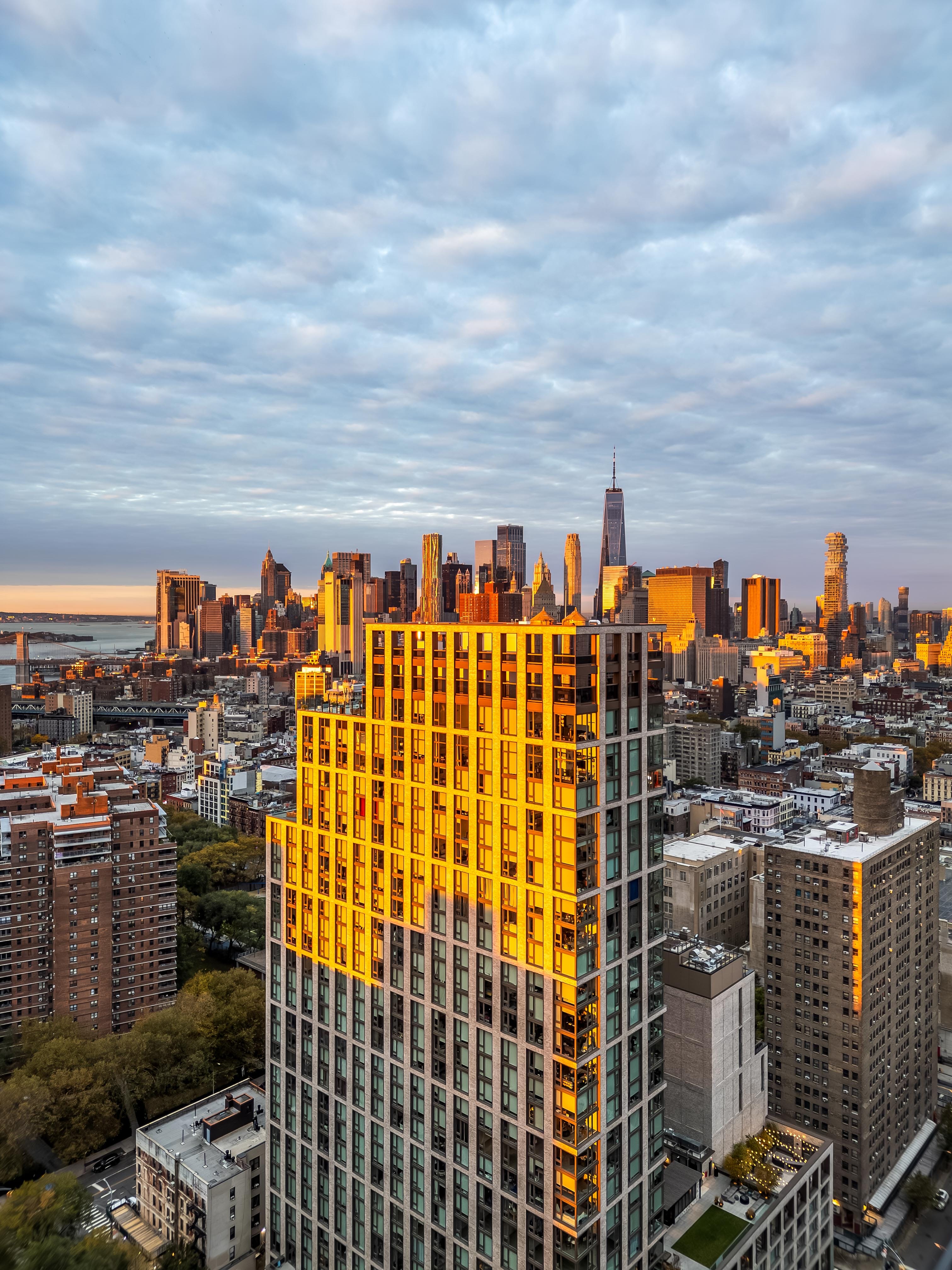 Elevated view of a sunlit residential tower with a distant skyline under layered clouds at The Suffolk in New York City
