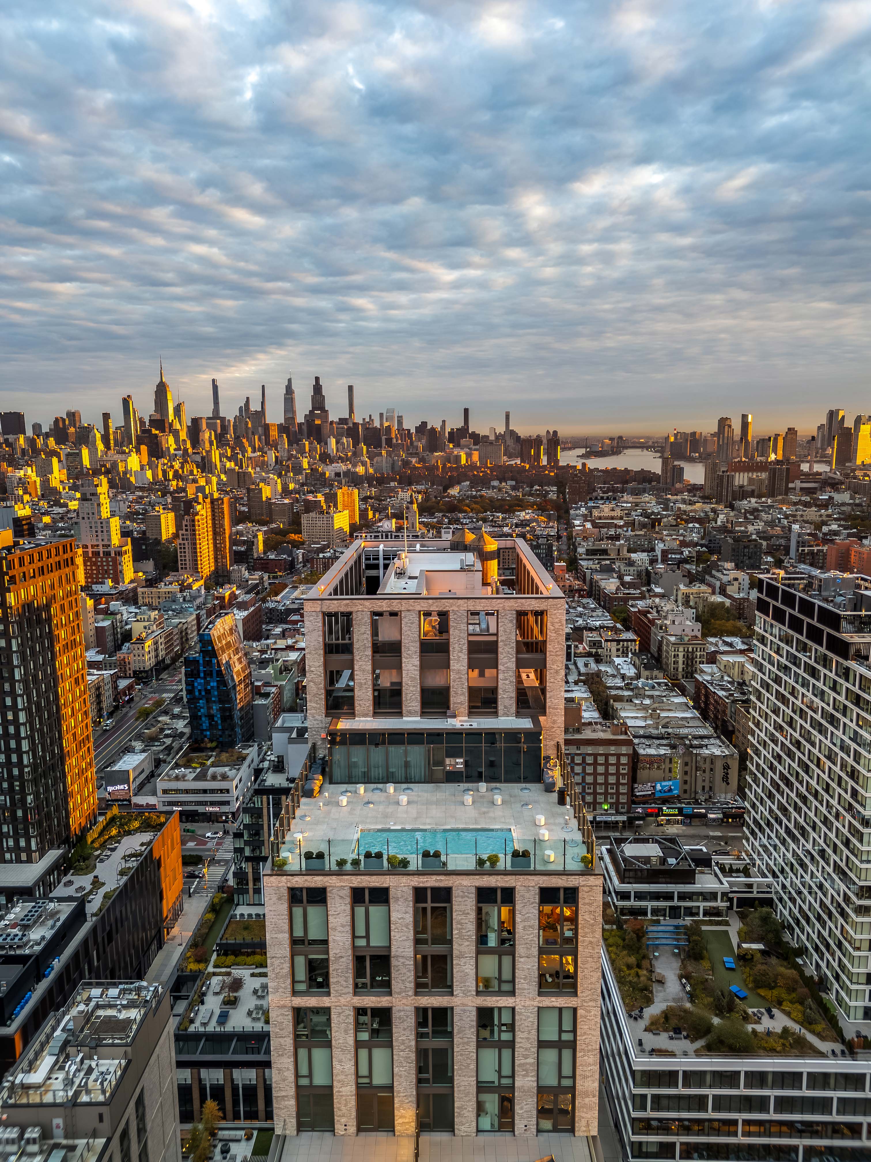 Elevated cityscape with rows of buildings, nearby rooftop pool, and dramatic cloudy sky at The Suffolk in New York City