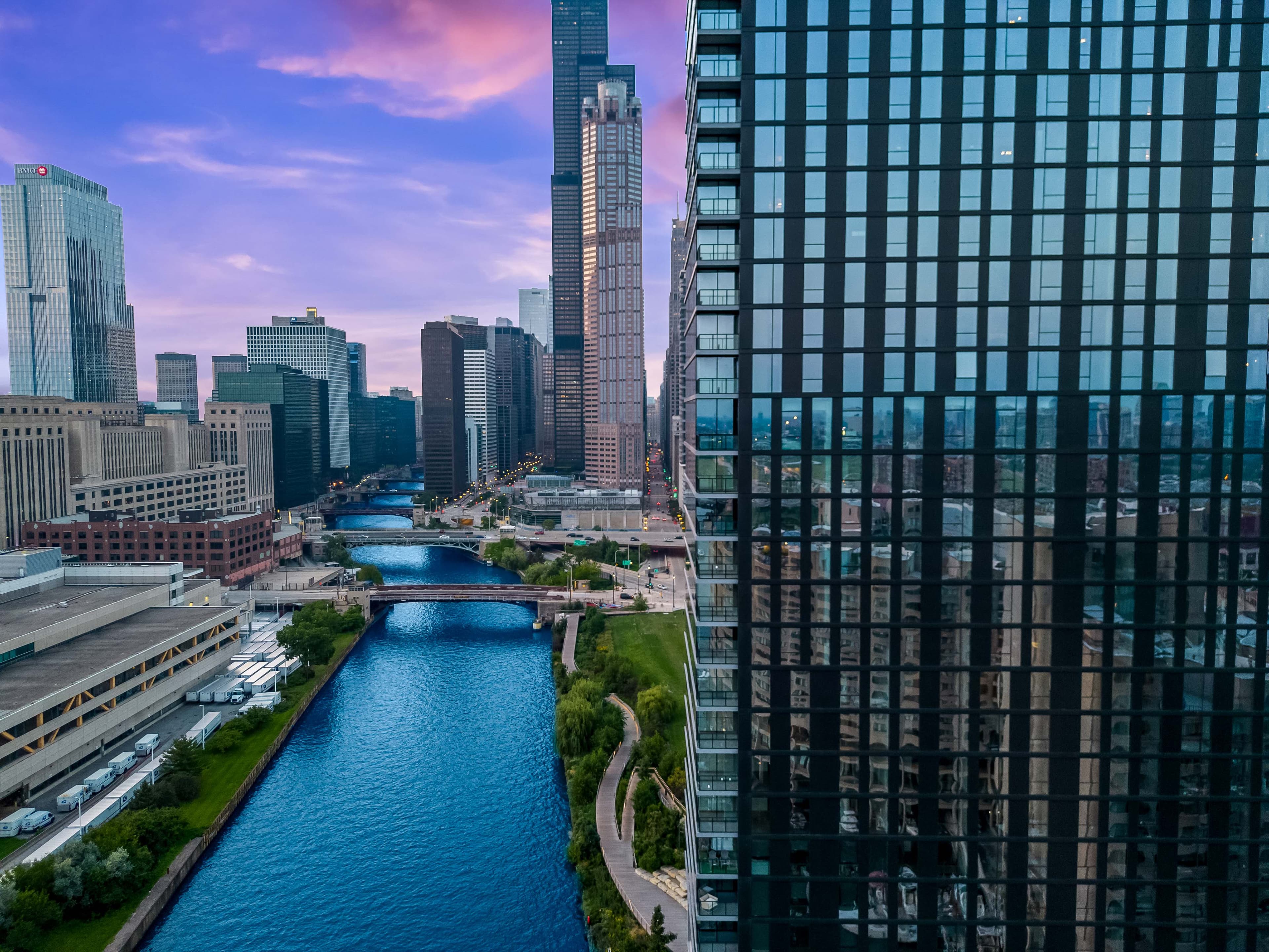 River winding between city buildings beneath purple sky beside glass tower at The Reed in Chicago