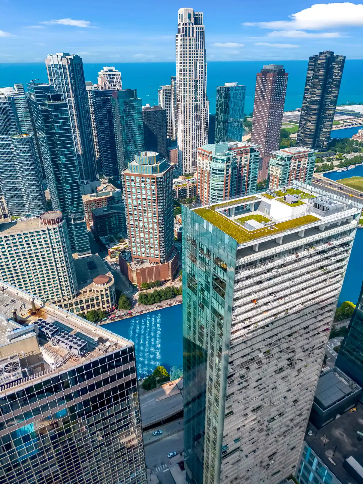 Elevated view across dense highrise buildings toward broad blue water beyond at Coast Lakeshore in Chicago
