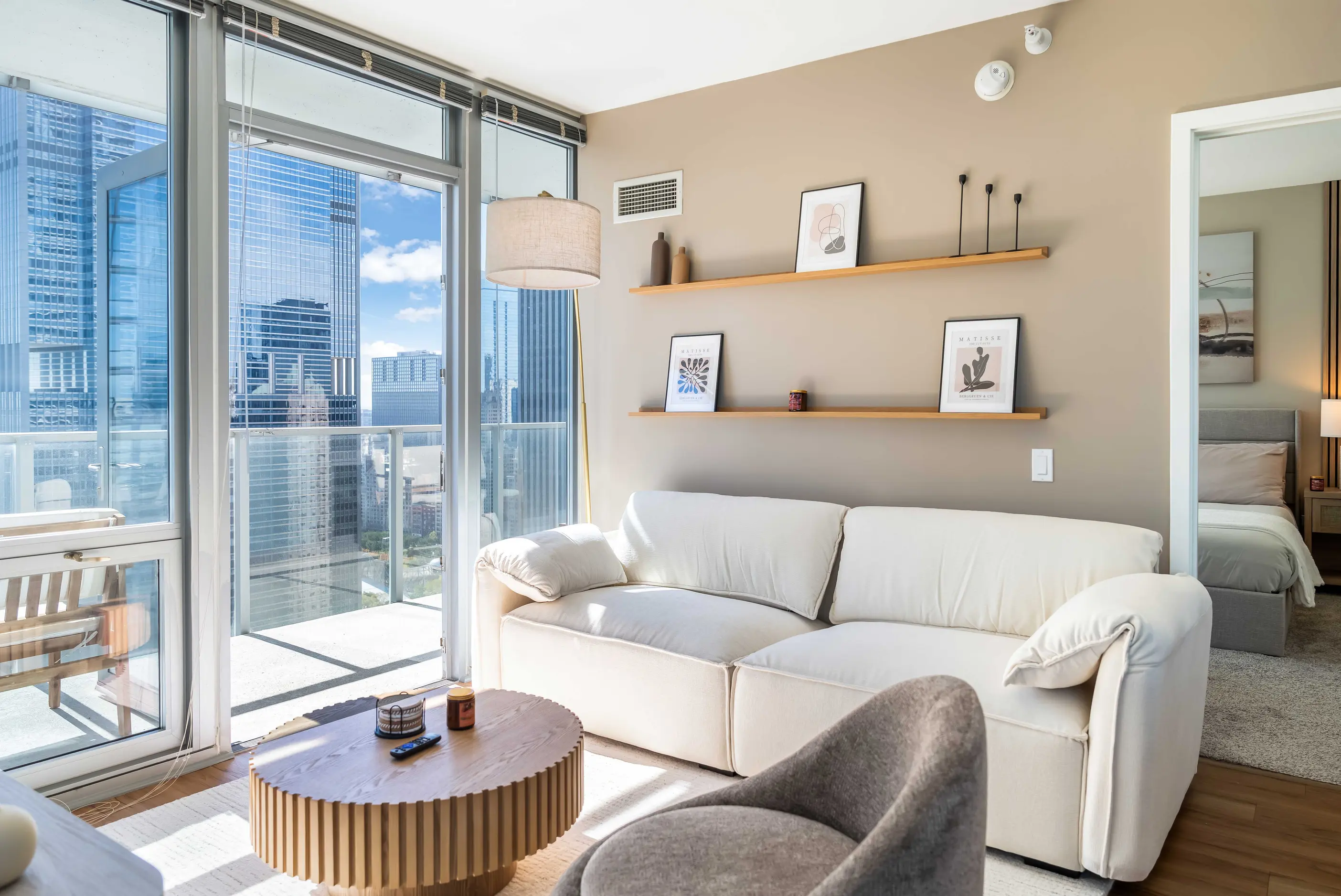 White sofa and table beside a gray armchair and glass doors opening onto balcony at The Atlas Highrise in Chicago