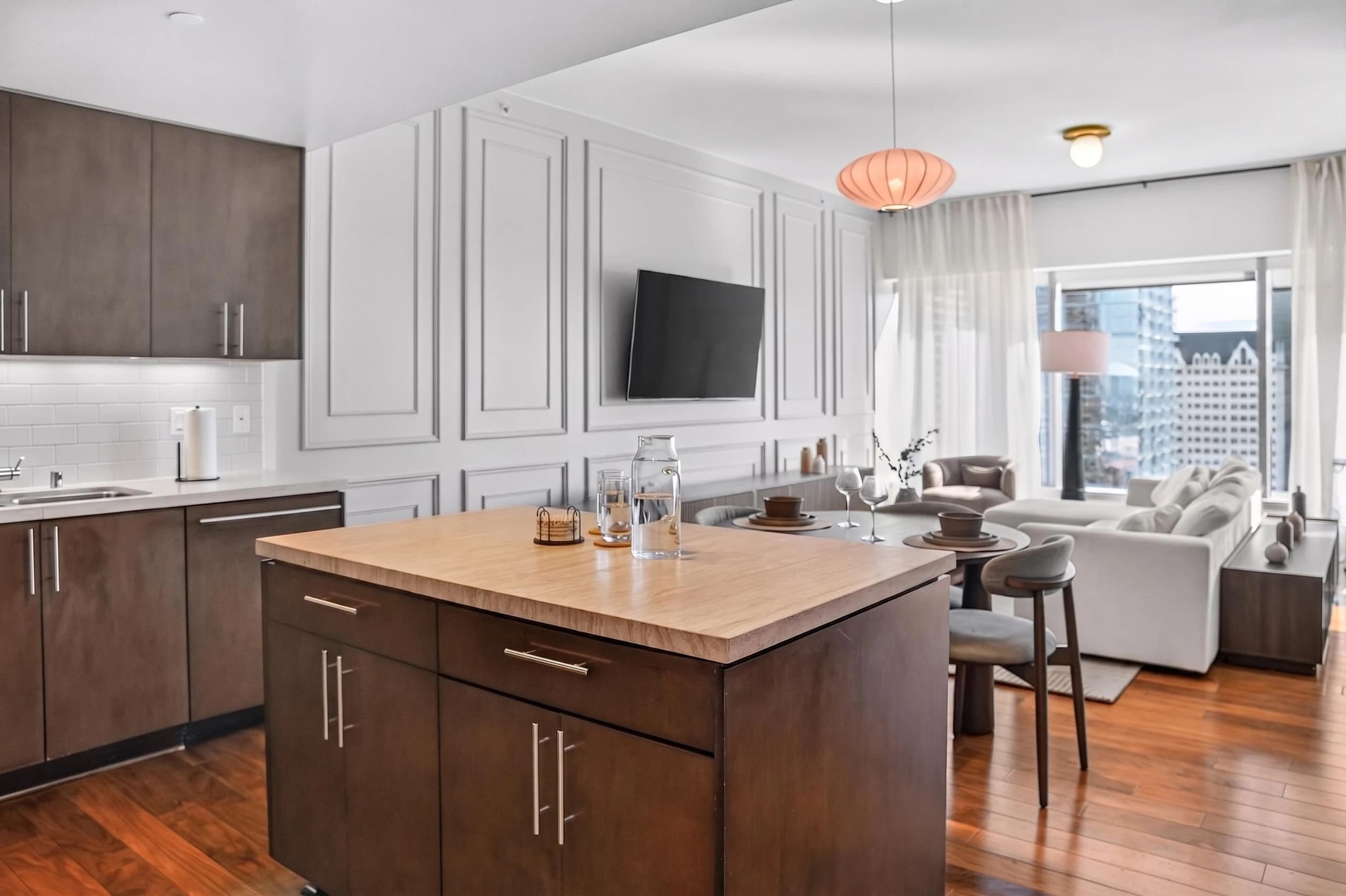 Kitchen island beside dining table and living room beneath orange hanging light at The Meridian Highrise in Los Angeles