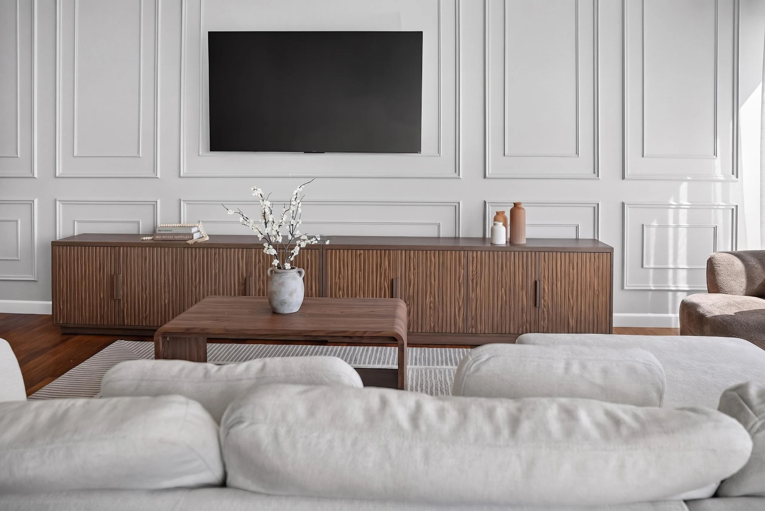 Living room with pale sofa facing a television inset into white paneled walls at The Meridian Highrise in Los Angeles