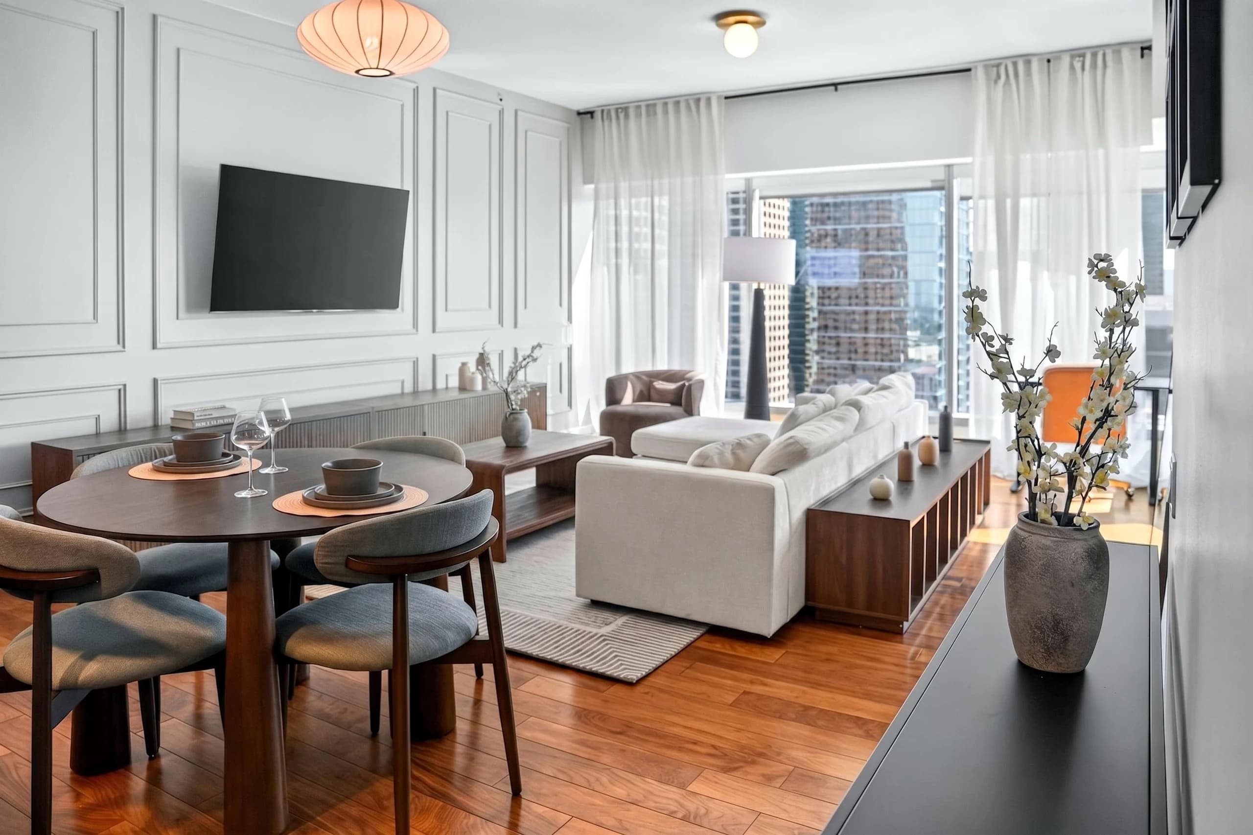 Living and dining area with pale seating, dark dining table, wall television, and broad curtains at The Meridian Highrise in Los Angeles