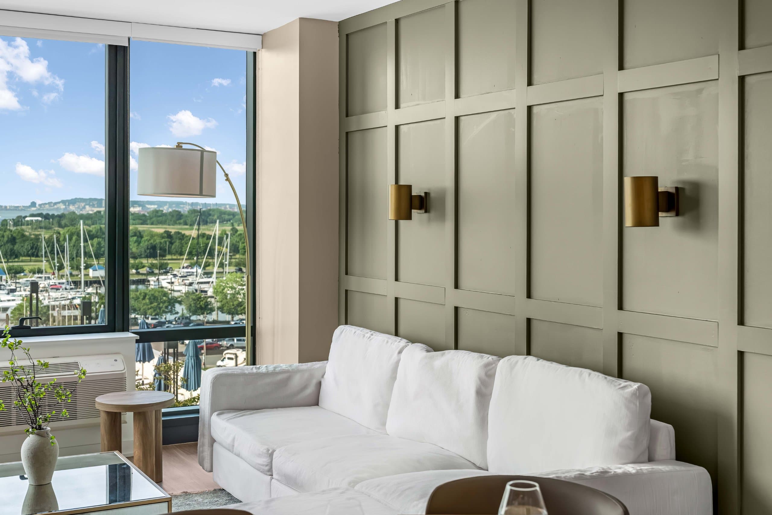 White sofa beneath green paneled wall beside floor lamp and balcony windows at The Metropolis in Jersey City