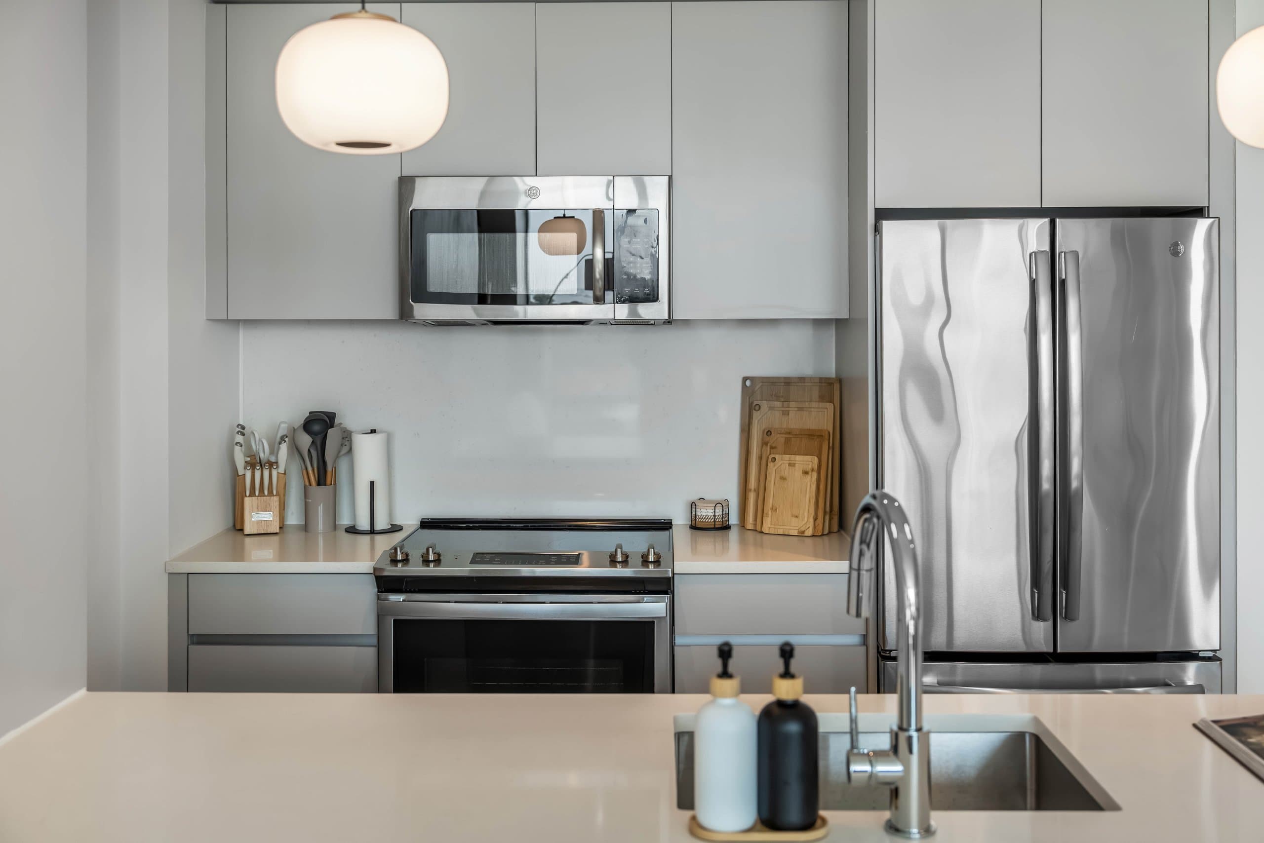 Kitchen island sink facing stainless stove and refrigerator beneath round pendant light at The Metropolis in Jersey City